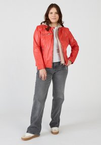 Röd läderjacka med dragkedja framtill, krämfärgad foder och sidofickor med dragkedja, matchad med grå jeans och vita sneakers.