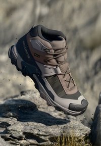 Braune und graue Wanderschuhe mit hohem Knöchel, Mesh- und Synthetikmaterial, Gummisohle, Schnürsystem und wasserdichter Gore-Tex-Kennzeichnung.