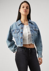 Light blue cropped denim jacket with button front, two chest pockets, and long sleeves; worn over a white fitted top and black jeans.