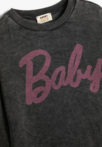 Sudadera gris oscuro con un cuello redondo, que presenta un prominente texto en cursiva color burdeos que dice "Baby." Fabricada con material suave y un acabado texturizado.