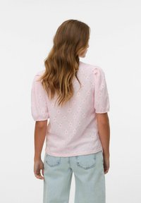 Ljusrosa blus med puffärmar, prydd med diamantformade hålmönster. Stylad med ljusblå jeans med hög midja, som visar strukturerad tyg.
