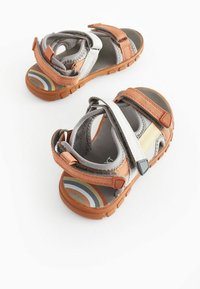 Grå og orange sandaler med velcro-stropper, der har en tekstureret gummisål og et flerfarvet stribet indersåledesign.