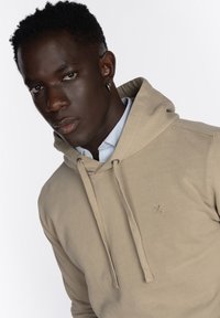 Sudadera con capucha de color beige, con cordones ajustables, material de algodón suave, puños acanalados y un pequeño logo en el pecho.