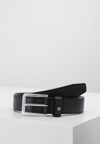 Cinturón de piel negra con un acabado texturizado, hebilla de metal plateado y un extremo de piel suave. Presenta un pequeño acento cerca de la hebilla.