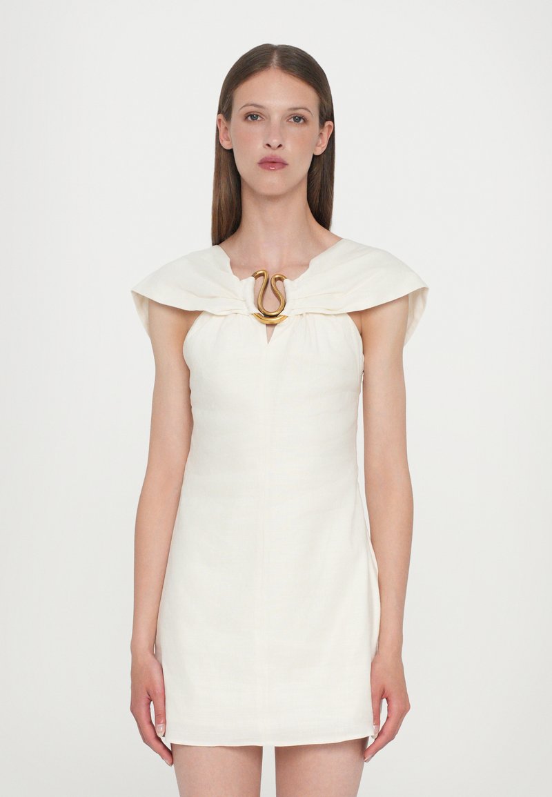 White linen dress with a fitted silhouette, wide cap sleeves, and a gold snake-shaped brooch at the neckline. Smooth texture, knee-length.