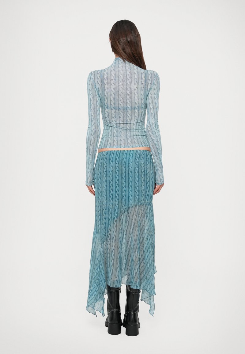 Woman wearing a blue patterned long-sleeve top and matching asymmetrical skirt paired with black mid-calf boots, standing facing away.