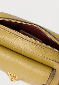 Mala de mão em couro amarelo suave com fecho de correr, forro interior cor de vinho e detalhes em metal dourado. Apresenta uma textura lisa e detalhe com logótipo.