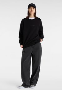 Sudadera negra con el logotipo "vans." en relieve, combinada con pantalones sueltos en gris oscuro. Para completar el look, lleva una gorra negra y zapatos de cuadros.
