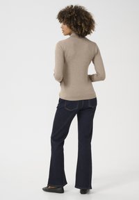 Maglione beige a collo alto con maniche lunghe, abbinato a jeans svasati blu scuro. L'outfit presenta un design aderente e un collo a coste.