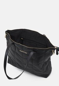 Black Valentino quilted tote bag with gold zipper and logo, featuring two handles and an open top showing an inner zip pocket.