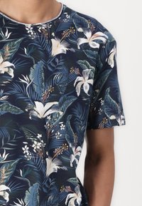 Tricou bleu marin cu mânecă scurtă, ce prezintă un imprimeu floral tropical cu crini albi și frunze verzi, fabricat dintr-un material moale și texturat.