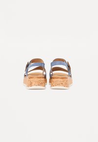 Sandali platform in sughero con straps in suede blu. Presentano un sottopiede in sughero texturizzato e una suola esterna in gomma bianca liscia. Due cinturini alla caviglia regolabili.