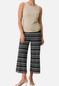 Haut sans manches beige à côtes avec des détails froncés, associé à un pantalon large noir présentant des motifs zigzag multicolores et une texture lisse.