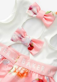 Weißes ärmelloses Kleid mit einem Rock aus pinkem Stoff mit Blumenmuster. Zwei rosa Schleifen auf der Rückseite; der Taillenbund ist mit "BAKER" in Weiß bedruckt. Goldener Reißverschluss.