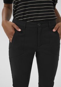 Black pants made of a smooth, stretchy fabric with a fitted design. Features a front button closure and side pockets, with a tailored look.