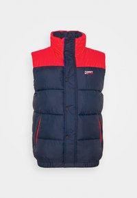 Tmavě modrá péřová vesta s červeným klínem, vysokým límcem a cvočky. Má boční kapsy a malý nápis "TOMMY JEANS" na hrudi.