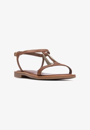 Sandalias de cuero marrón con un diseño minimalista que incluye dos finas tiras y un detalle metálico. La suela plana tiene un acabado texturizado.