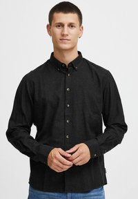 Shirt nera a maniche lunghe in tessuto testurizzato, con colletto button-down e bottoni a contrasto. Taglio attillato con bottoni ai polsi.