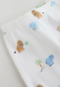 Tissu blanc côtelé avec des motifs animaux colorés, notamment des lions, des éléphants et des arbres, avec une texture douce et une ceinture élastique.
