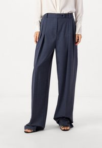 Weite marineblaue Hose aus strukturiertem Stoff, mit vorderen Falten, Knopfverschluss und Gürtelschlaufen. Geeignet für verschiedene Anlässe.