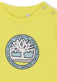 Geel katoenen t-shirt met een ronde grafiek met een gestileerde boom in wit en blauw, gemarkeerd met "Timberland" en "Klaar voor het Grote Buiten".