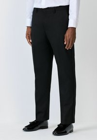 Schwarze formelle Hosen mit schlanker Passform, aus glattem Stoff gefertigt. Verfügt über eine flache Vorderseite, Gürtelschlaufen und Seitentaschen, kombiniert mit glänzenden schwarzen Schuhen.