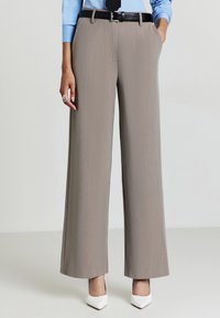 Pantaloni a gamba larga in morbido tessuto grigio con una sottile texture, dotati di tasche e di una cintura nera. Abbinati a décolleté bianche a punta.