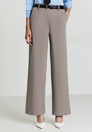 Pantaloni a gamba larga in morbido tessuto grigio con una sottile texture, dotati di tasche e di una cintura nera. Abbinati a décolleté bianche a punta.