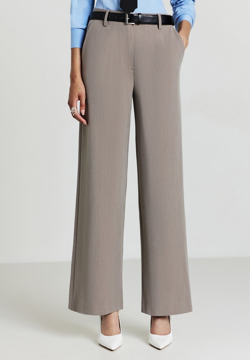 Pantaloni a gamba larga in morbido tessuto grigio con una sottile texture, dotati di tasche e di una cintura nera. Abbinati a décolleté bianche a punta.