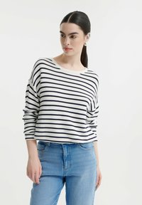 Gestreepte longsleeve top in wit en marineblauw. Geribbelde textuur, ronde halslijn, relaxed fit, gecombineerd met lichtblauwe denimjeans.