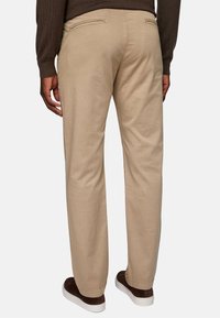 Beige chinos with a straight leg, made of a smooth fabric. Features back pockets and worn with dark brown sneakers.