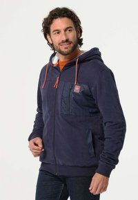 Marineblauwe zip-up hoodie met oranje trekkoorden, fleece-voering in de capuchon en een gewatteerde borstzak. Heeft ribgebreide manchetten en een ontspannen pasvorm.