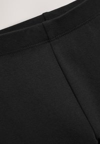 Bukser med sort elastisk linning og en glat, mat tekstur. Indeholder enkel syning og et tætsiddende design uden yderligere detaljer.