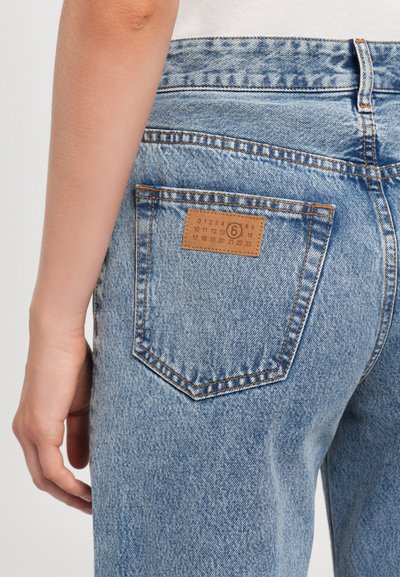 Light blue denim jeans feature a back pocket with a brown leather label, contrasting stitching, and a relaxed fit with a slight distressed texture.