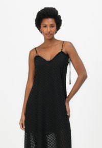 Black dress made of textured fabric with a V-neckline, thin straps, and an A-line silhouette, featuring a subtle dot pattern.