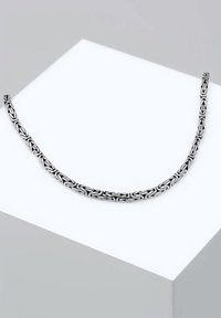 Collana a catena in argento con un disegno intricato di maglie ovali, caratterizzata da una texture liscia e una superficie riflettente, esposta su un piedistallo bianco.