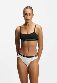 Sort bralette med tynde stropper og et gråt HUGO-bånd; hvid thongedragt med en sort HUGO-linning; glat stof, minimalistisk design.