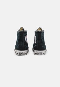 Czarne trampki z wysoką cholewką wykonane z płótna, z gumową podeszwą. Posiadają białą okrągłą naszywkę z logo oraz branding "Converse All Star" na pięcie.