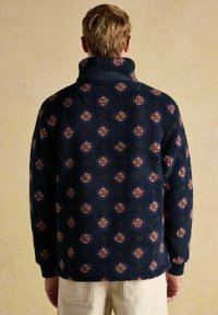 Marineblauer Fleece-Pullover mit hohem Kragen, der ein florales Muster in Pink und Lila aufweist, eine strukturierte Oberfläche und elastische Bündchen hat.
