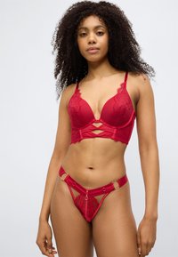 Σετ κόκκινου εσωρούχου που περιλαμβάνει σουτιέν με δαντέλα και βαθύ ντεκολτέ με κοψίματ α, σε συνδυασμό με τανγκάκι που διαθέτει λεπτομέρειες με κρίκους.
