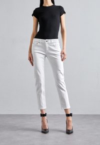 Valkoiset farkut, joissa on slim fit ja lyhyt pituus, yhdistettynä mustaan istuvaan t-paitaan ja mustiin korkeisiin korkokenkiin. Sileä rakenne, klassinen muotoilu.