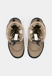 Bottes de style puffer beiges avec une semelle en caoutchouc noire, dotées d'un système de fermeture à cordon et d'un intérieur doux. Marquage visible sur le côté.
