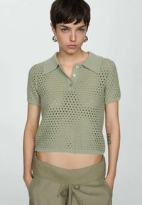 Polo shirt verde chiaro, corto, con maniche corte, caratterizzato da un motivo lavorato a maglia con fori e chiusura a tre bottoni. Tessuto liscio.