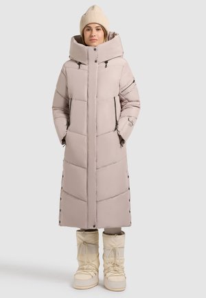 Lichtbeige pufferjas met een hoge kraag en verticale gestikte patroon. Voorzien van twee zijzakken en zwarte ritsen. Gepaarde met crèmekleurige laarzen.