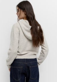 Vaaleanharmaa fleece-huppari, jossa on nyörit, ribbireunus ja tasku edessä, yhdistettynä tummansinisiksi farkuiksi, joissa on takataskut.