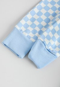 Blå rutigt tyg med lång ärm och ljusblå ribbade muddar. Materialet verkar mjukt och lätt, med ett kontrasterande färgmönster.