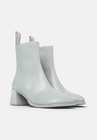 Par de botines de cuero gris claro con tacones cuadrados y tiradores, mostrados en un ligero ángulo sobre un fondo blanco.