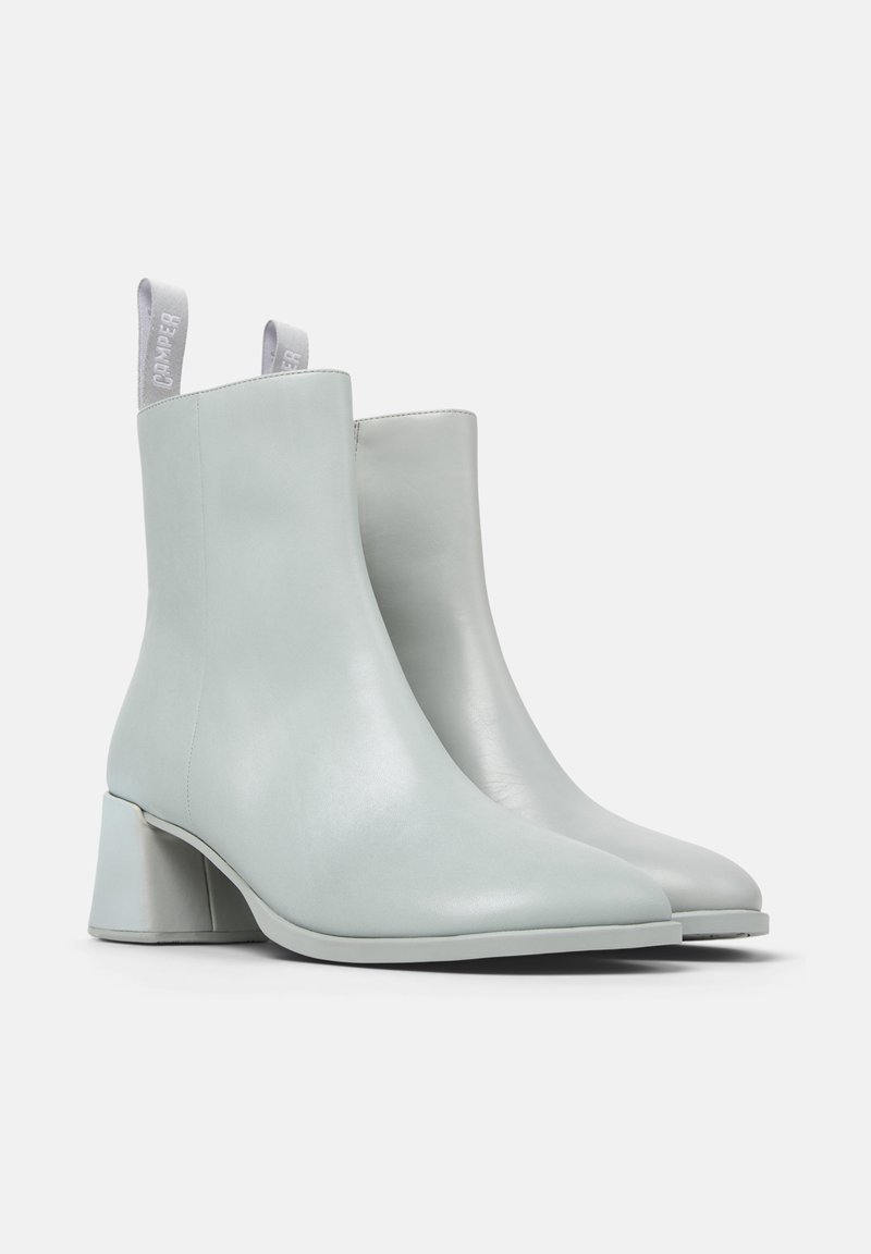 Een paar lichtgrijze leren enkellaarzen met blokhakken en aantreklusjes, getoond in een lichte hoek op een witte achtergrond.