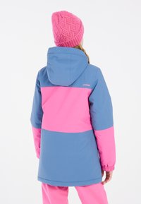 Chaqueta de esquí colorida con paneles azules y rosas, capucha desmontable, puños elásticos y marca en la parte posterior. Gorro de punto grueso color rosa.