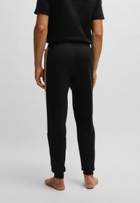 Black sweatpants with a fitted waist and cuffs, featuring tan and white side stripes. Made from soft fabric, designed for comfort and mobility.